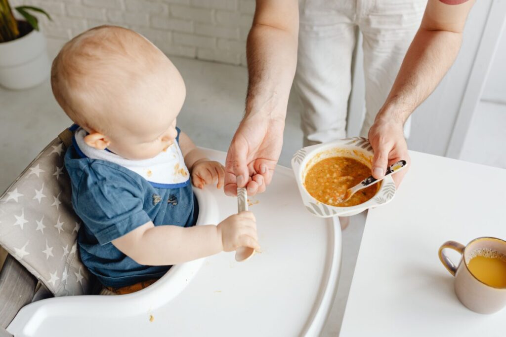 A happy baby sitting in a high chair trying a new solid food, representing the safe introduction of allergens to babies.