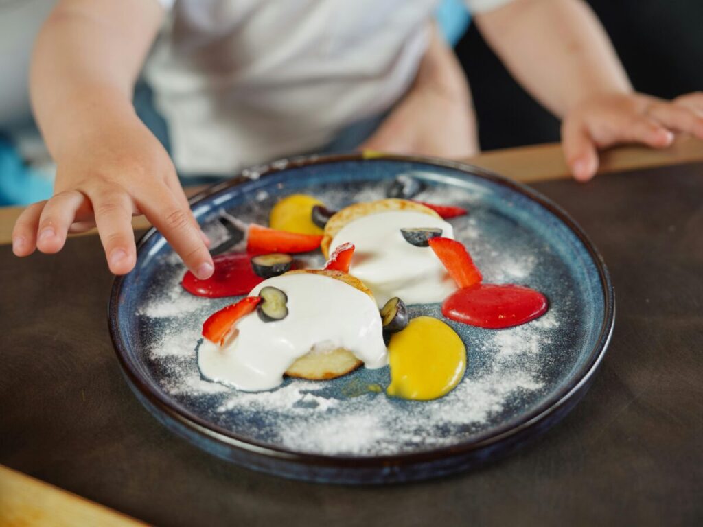 A toddler eating from a deconstructed plate with separate sections for different foods