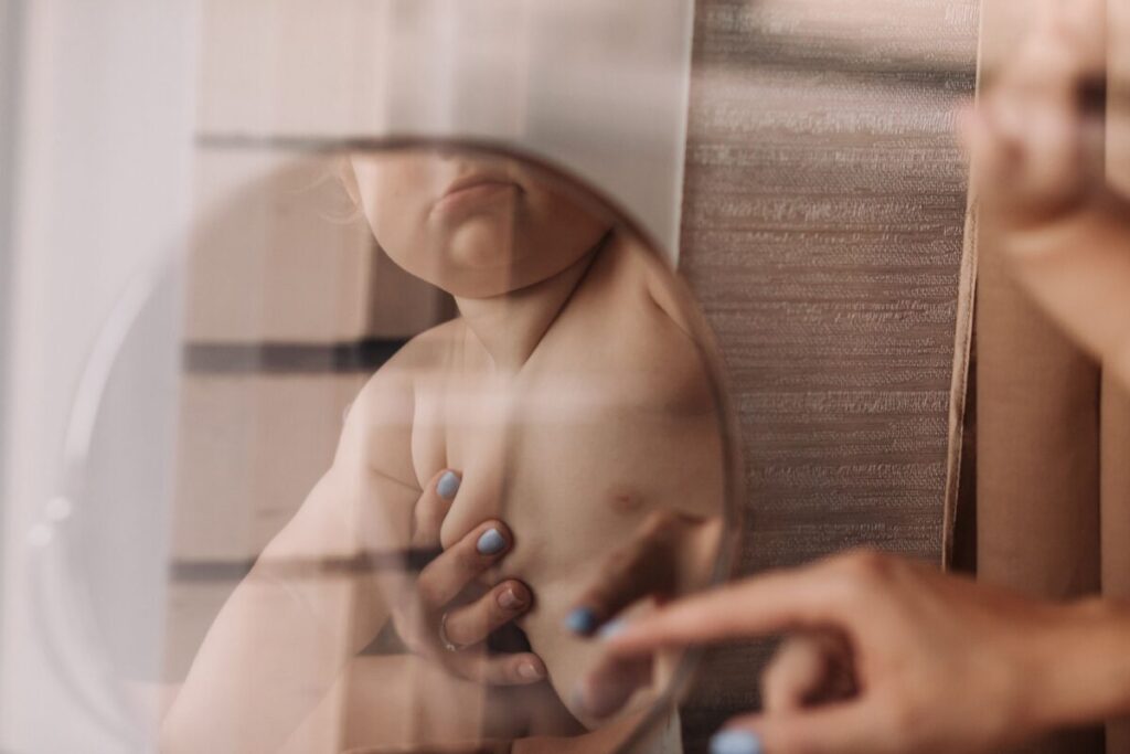 A happy 5-month-old baby smiling at their own reflection in a shatterproof mirror, engaging in simple activities for babies who can't crawl yet