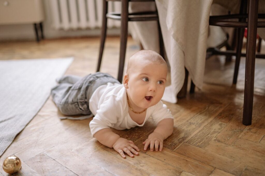 A curious 5-month-old baby lying on their tummy on a soft rug, actively playing with colorful toys, representing safe and engaging activities for this development stage
