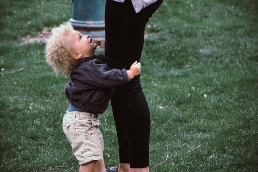 A deeply attached toddler hugging his mom's leg tightly, showing a common struggle when learning how to handle 21 month old separation anxiety