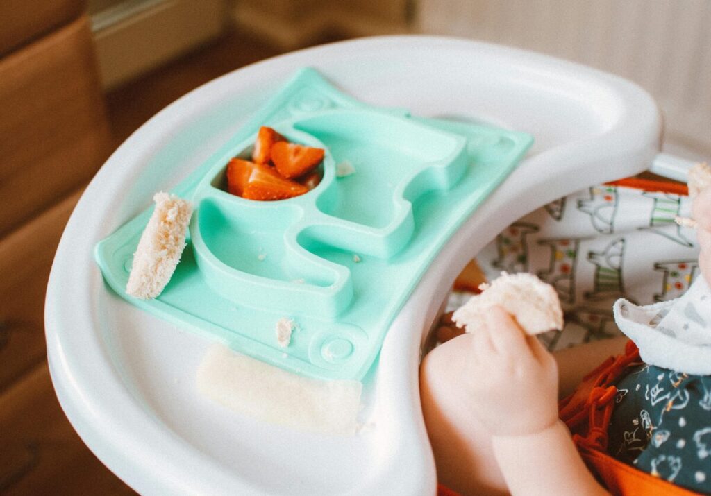 A 16-month-old toddler playing with finger foods instead of eating, illustrating a typical 16 month old feeding schedule struggle