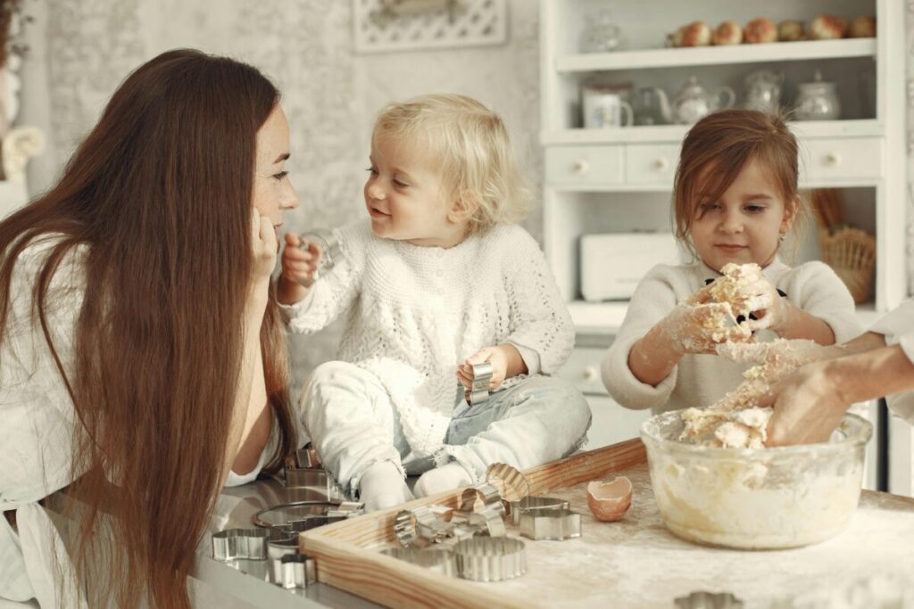 A relatable parent holding a baby in a messy kitchen, representing the humanly messy reality of summer teething