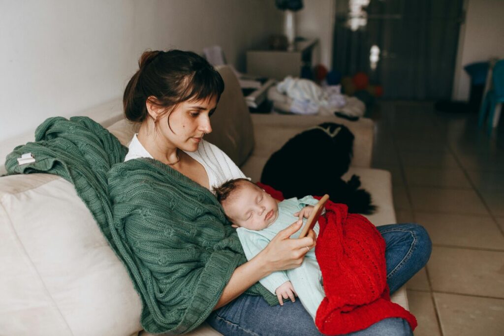 Exhausted mother sitting on the floor while a toddler pulls on her shirt, representing the mental and physical demands of motherhood.