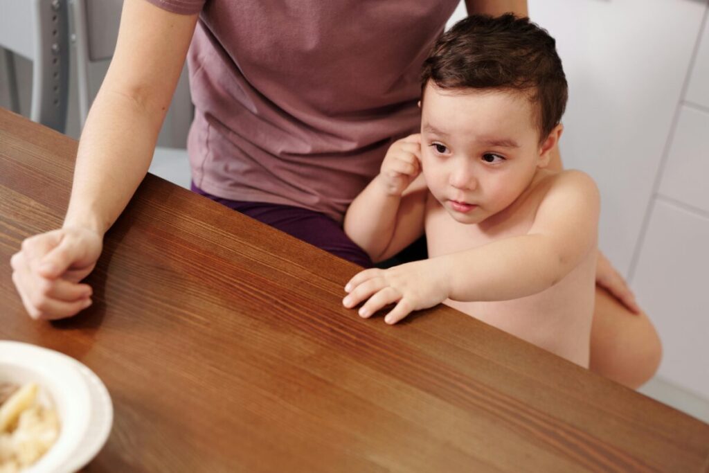 A frustrated toddler turning his head away and refusing to eat at 14 months in his high chair