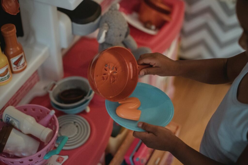 A 20-month-old child happily exploring and playing with safe plastic Tupperware containers and a wooden spoon on the kitchen floor