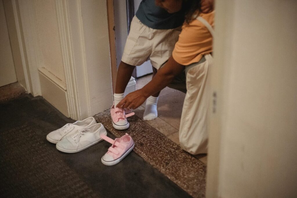 A stubborn two year old toddler testing boundaries by trying to put on shoes independently during a daily routine