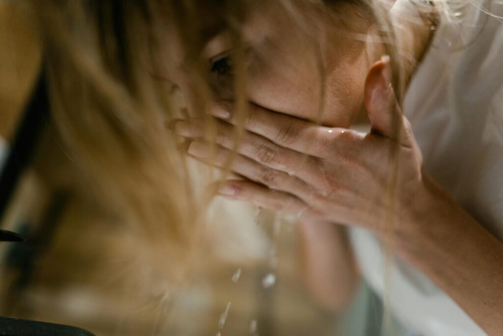 Stressed mom using simple sensory hacks like splashing cold water on her face to handle overstimulation and burnout.