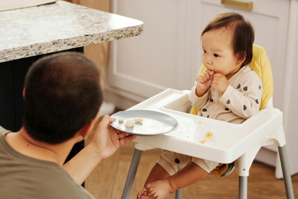 A toddler turning their head away and pushing a plate, showing what to feed a 16 month old who refuses to eat.
