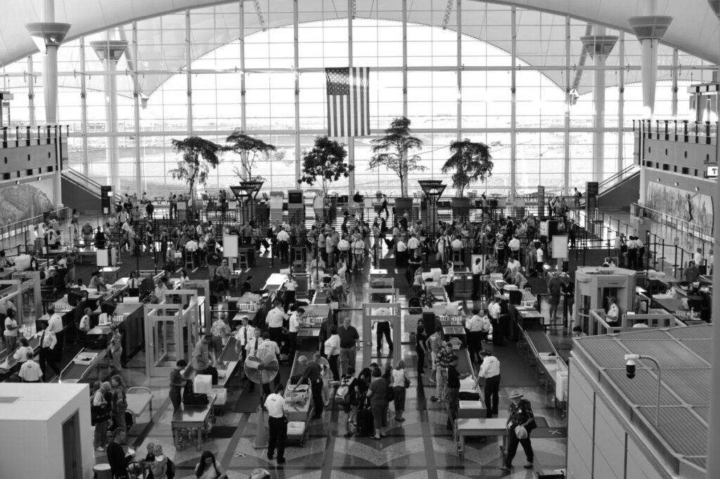A parent struggling to collapse a stroller at airport security while practicing tips for flying with an infant alone or with a partner