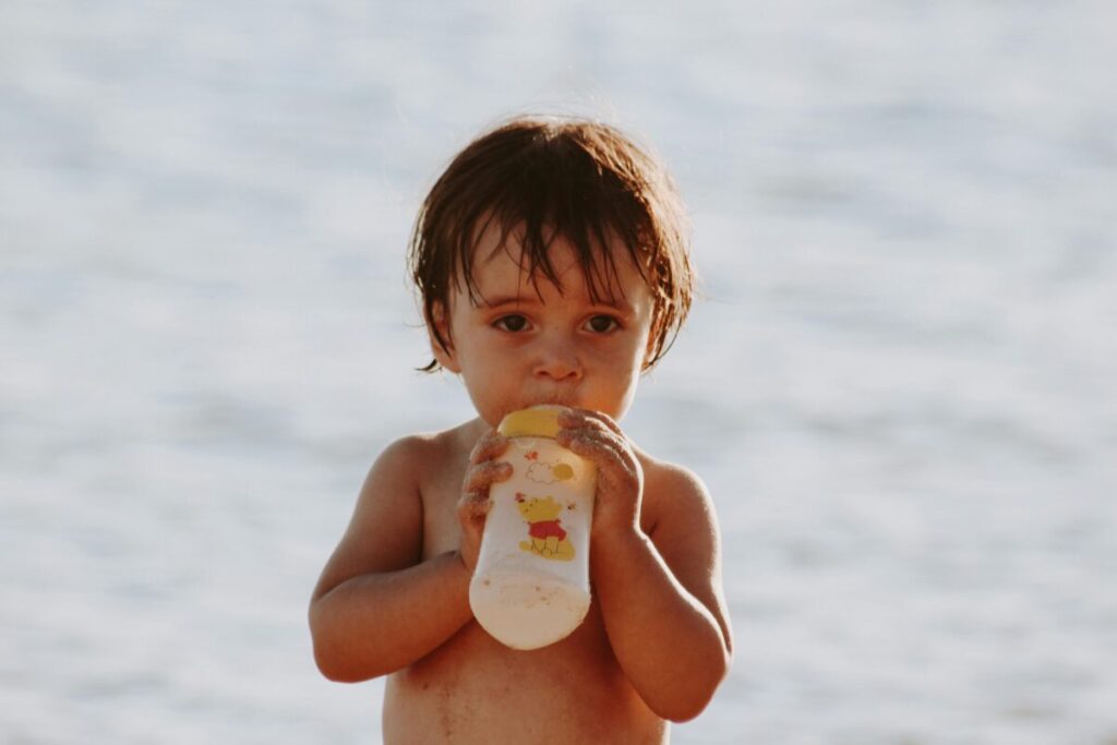 is toddler milk necessary - a happy toddler sitting in a kitchen high chair next to a tin of formula and a bottle of fresh whole milk