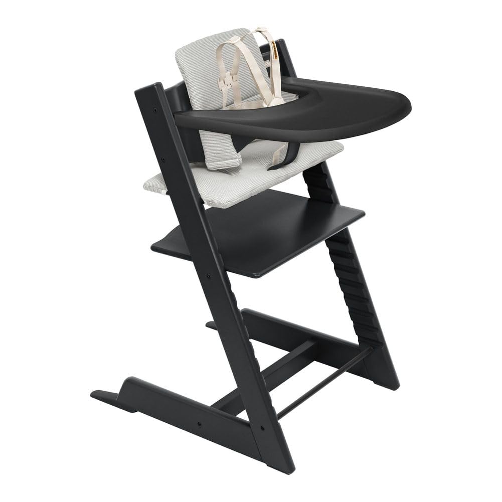 Black Stokke Tripp Trapp high chair in a realistic home kitchen with a 16-month-old toddler eating messily, used as a splurge investment for easy cleaning.