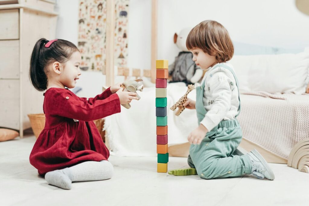 Two toddlers sitting next to each other on a rug participating in parallel play at the park