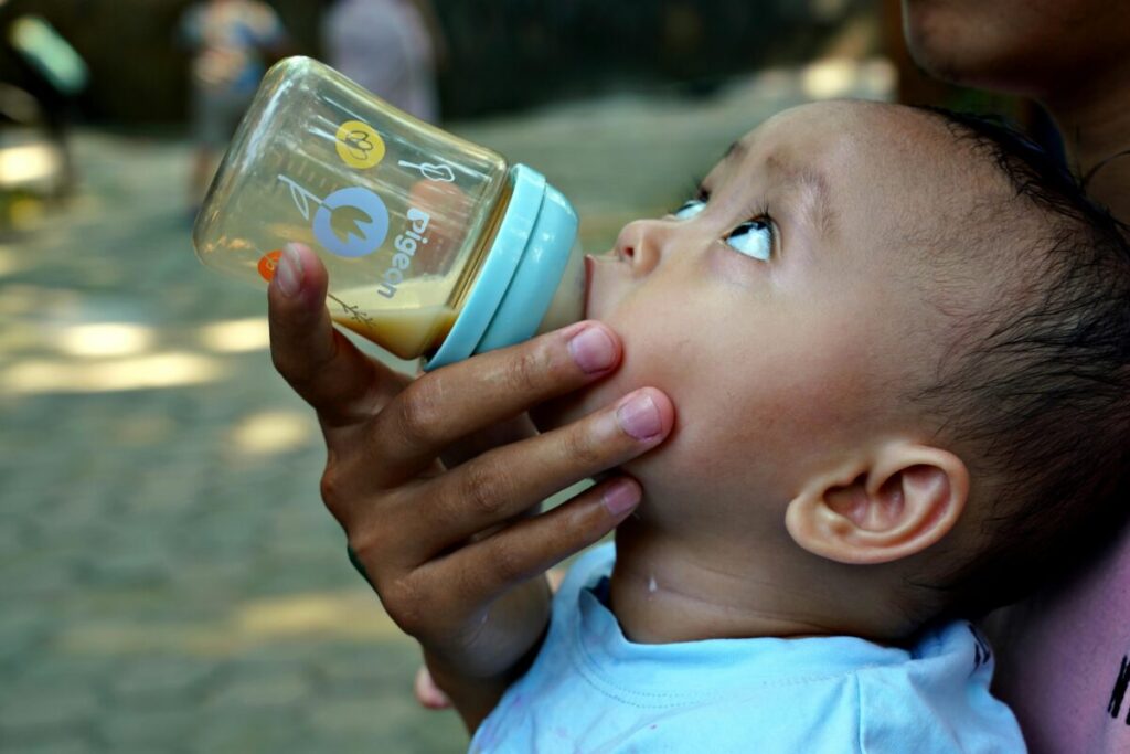 A 13-month-old toddler successfully drinking milk from a colorful straw cup
