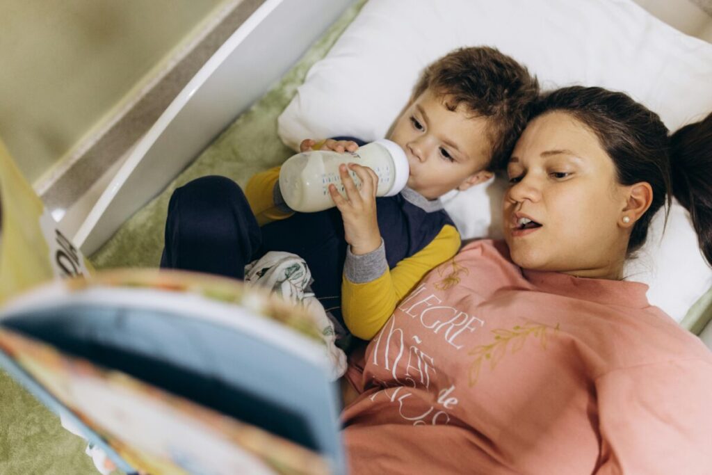 A cozy toddler happily drinking milk from a weighted straw cup in bedroom, showing how to drop the bedtime bottle on a 15 month old feeding schedule.