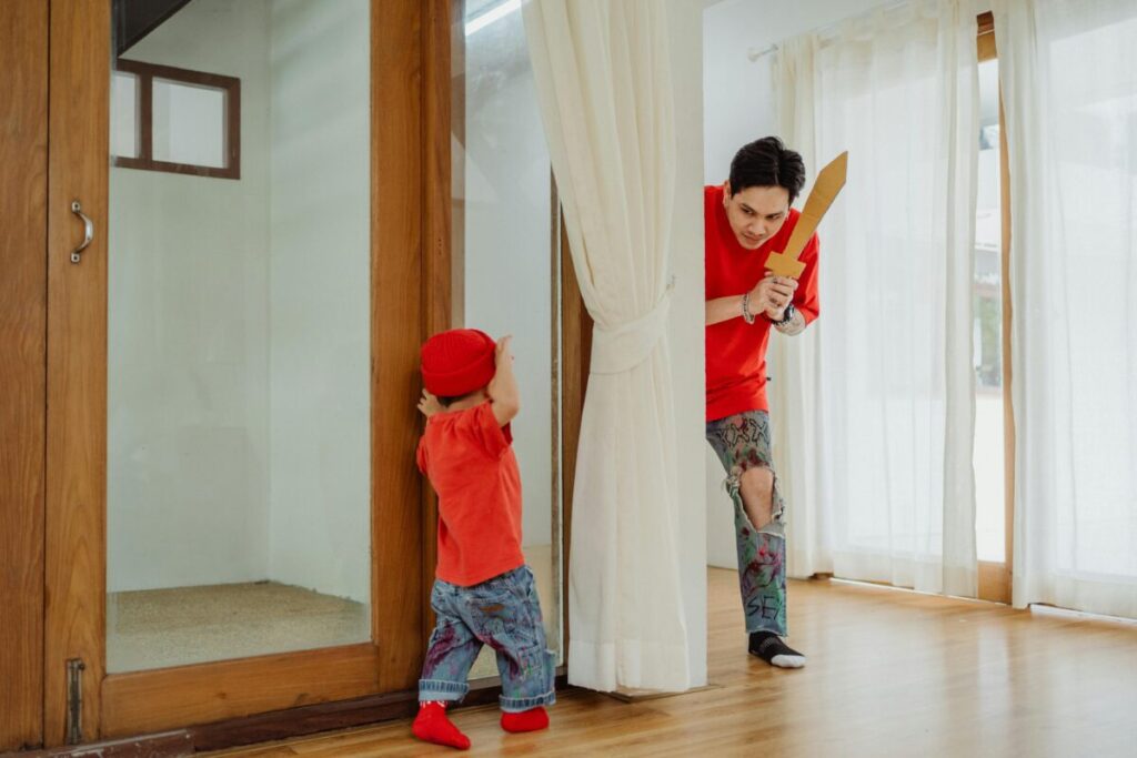 A toddler hiding behind curtains, showing early readiness signs for potty training at 2 years old
