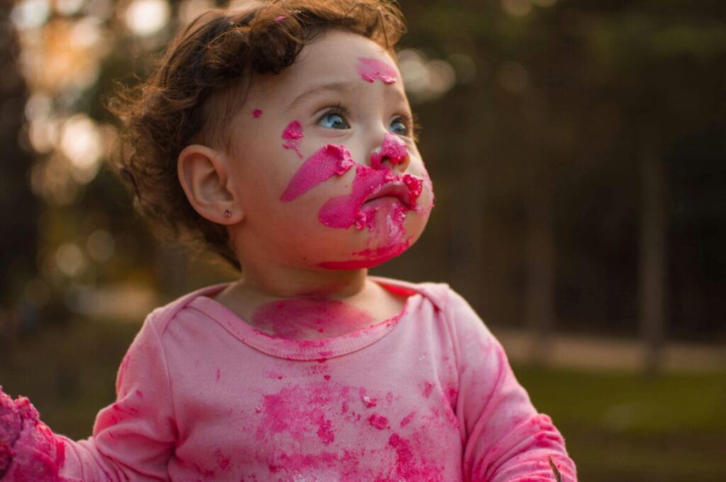 A messy toddler covered in food while playing at the dinner table, a common challenge when studying how to handle 19 month old picky eating patterns