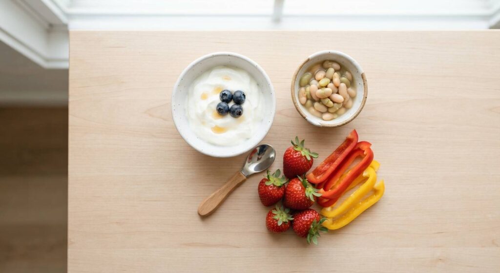 Assortment of immunity-boosting foods for toddlers including yogurt, beans, colorful vegetables, and berries on a wooden surface.